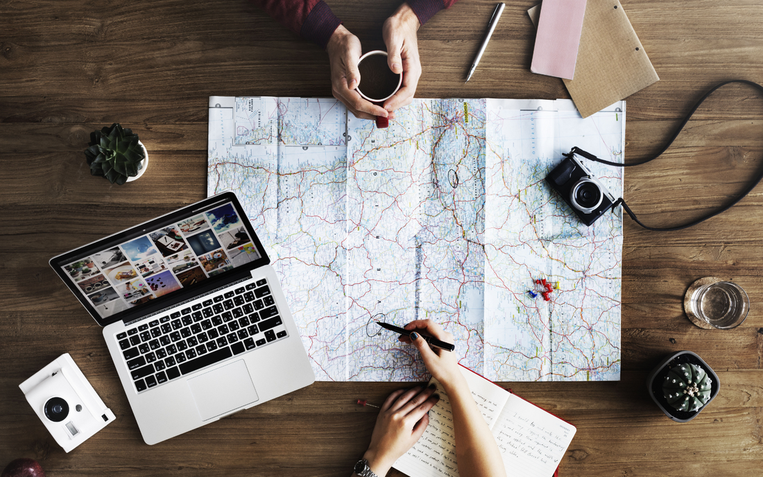 Overhead photo of two people with a map and laptop planning a trip